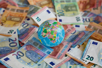 A globe with focus on Africa and Europe is lying on top of many different Euro banknotes. 