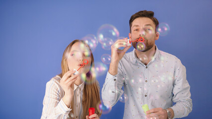 Soap bubbles on CAM. Man and woman are having fun with soap bubbles. Isolated on blue. High quality photo