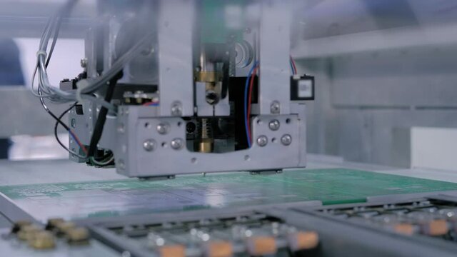 Automatic SMD pick and place machine during work - assembly of computer printed circuit board at factory. Automated technology, industrial, robotic, electronic, production, manufacturing concept