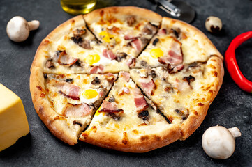 Pizza carbonara with bacon, cheese, mushrooms, quail eggs, creamy sauce on a stone background