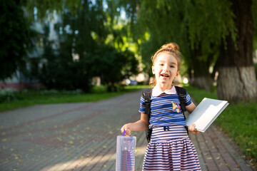 A little girl of Caucasian appearance in a school uniform with a backpack and the book and a set of markers. back to school. Elementary school, developing activities for preschoolers. Space for text