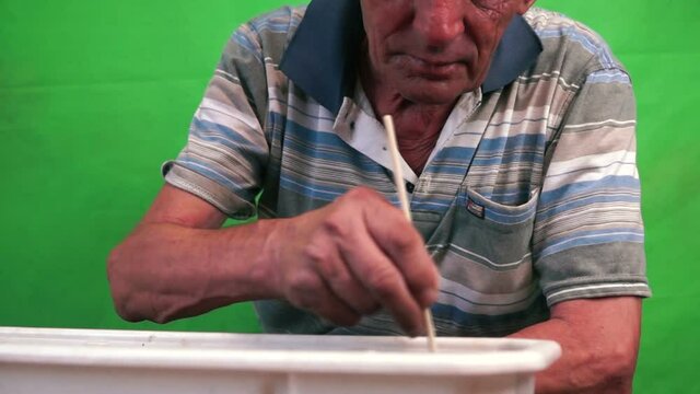 Concept on the topic of a hobby for retirees. A Caucasian male over 70 years old is caring for the seeds of seedlings by cultivating the land in a plant pot. Plant care. Green Screen Selective Focus