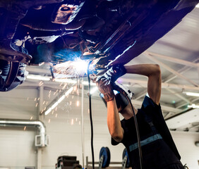 Car mechanic with protective mask welding car. Service station