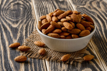 Whole raw almonds in a beige ceramic bowl on a dark wood table. Unroasted nuts as antioxidant and protein source for ketogenic diet and vegetarianism. Healthy eating.