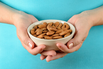 Caucasian woman hands hold beige ceramic bowl with raw almonds. Unroasted nuts as antioxidant and...