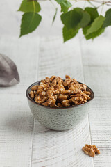 A walnut in a bowl on a light wooden table with green leaves in the background. Healthy snacks, healthy food. Nuts.