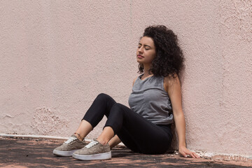 Fototapeta na wymiar Latin woman sitting and leaning against a pink wall. girl sunbathing with curly hair