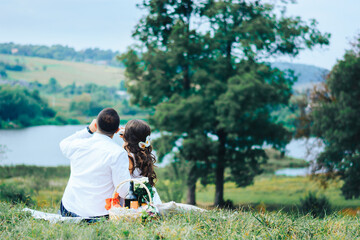 Beautiful couple drinking wine at a picnic by the lake. Honeymoon concept. Rear view. Place for text