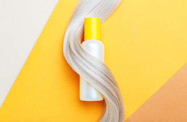 Shampoo bottle mockup strand in lock curl of blonde hair on orange color background. Yellow bottle shampoo. Flat lay copy space. Hair care cosmetics bath beauty products hair treatment