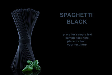 Black spaghetti with basel leaves on black background and place for text