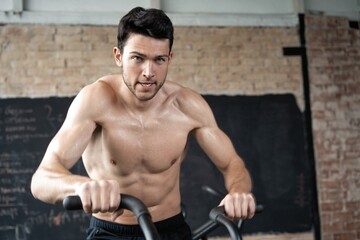 Obraz premium Man using exercise bike at the gym. Fitness male using air bike for cardio workout at Functional training gym.