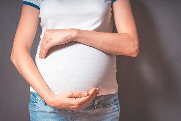 Pregnant woman holds hands on belly on a gray background. pregnancy, motherhood, people and expectation concept. Close-up, copy space, indoors. Toned photo of pregnancy.
