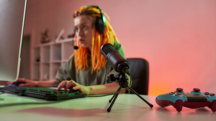 Fototapeta na wymiar Female esport gamer, woman in headphones looking focused, playing online video game on PC while recording, filming vlog. Focus on microphone