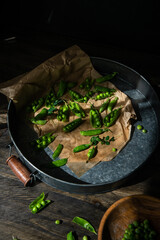 Fresh green pea pods on brown paper in metal tray.