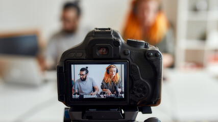 Woman with dreadlocks singing and playing. Female and male blogger recording making music using synthesizer, drum pad machine. Focus on camera screen