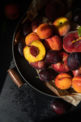 Tray full of fresh peaches, apricots and plums on dark background.