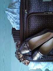 Open brown suitcase with women"s clothing for trip in the room