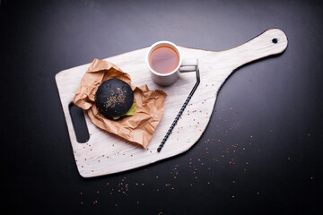 Black bread roll with black sesame held in hands over a kraft paper in human hands black background. Above view of strange black hamburger bread. Halloween food