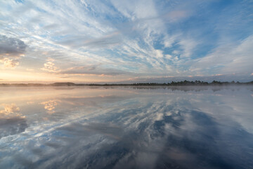 Sunrise rose-pink light in raised bog. Kakerdaja raised bog wetland in Estonia. Sunset glow over marsh hollows.  Symmetry created by reflection of trees and colorful clouds in moorland lake.
