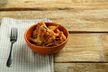 Brown cup with soba noodles with vegetables and chicken wings on a napkin and a fork nearby.