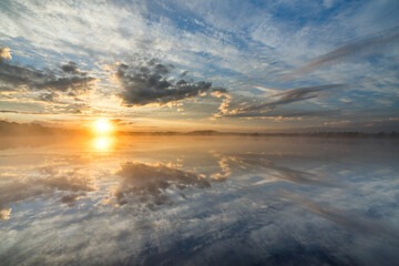 Sunrise rose-pink light in raised bog. Kakerdaja raised bog wetland in Estonia. Sunset glow over marsh hollows.  Symmetry created by reflection of trees and colorful clouds in moorland lake.
