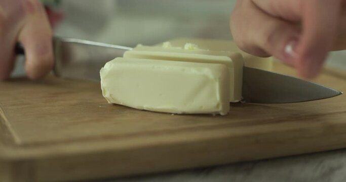 Female hands cut the butter with knife on wooden cutting board. Close up