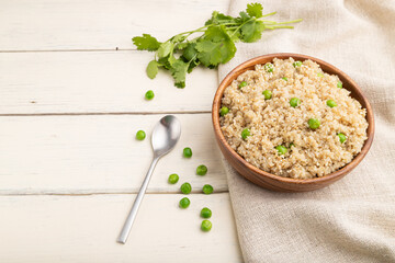 Quinoa porridge with green pea in wooden bowl on a white wooden background. Side view, copy space.