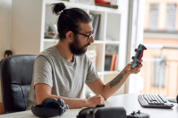 Male technology blogger in glasses looking at game controller joystick, holding it while recording...