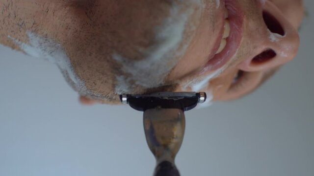 A man shaves his beard with a razor and shaving cream-close-up. A first-person camera attached to a shaving machine.