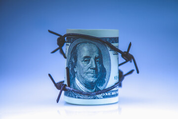 Close up barbed wire and US Dollar bill as symbol of economic warfare, sanctions and embargo busting.
