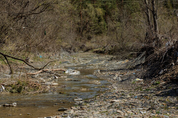 A beautiful small stream is littered with a bunch of garbage, empty bottles, cellophane bags, plastic cans