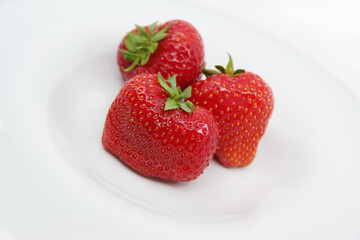 Three red ripe strawberries on a white plate. Strawberries isolated on a white background.