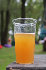 
A plastic glass with beer stands on a wooden table in nature