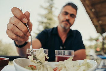 Adult man eating salad outdoors.