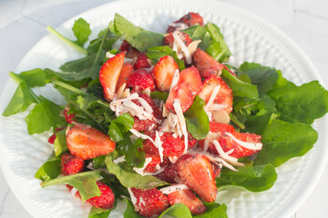 Summer salad with strawberries on a white plate and a light background. Place for copy space