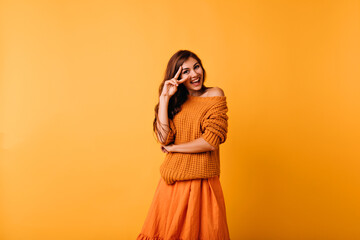 Stunning caucasian girl in trendy orange sweater smiling to camera. Indoor photo of wonderful young woman wears bright clothes.