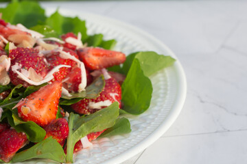 Summer salad with strawberries on a white plate and a light background. Close up. Place for copy space