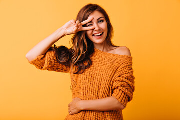 Blissful stylish girl posing with peace sign on yellow background. Studio photo of well-dressed...