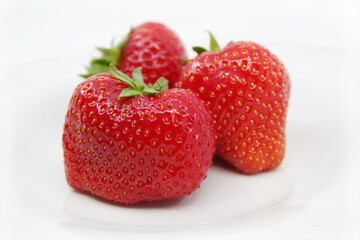 Three red ripe strawberries on a white plate. Strawberries isolated on a white background.