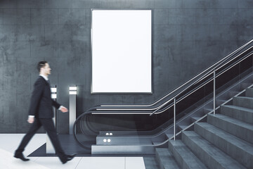 Train station interior with businessman climbing escalator and blank billboard
