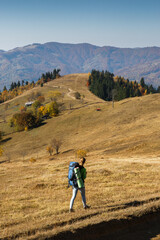 Female hiker with big backpack walking in mountains in autumn
