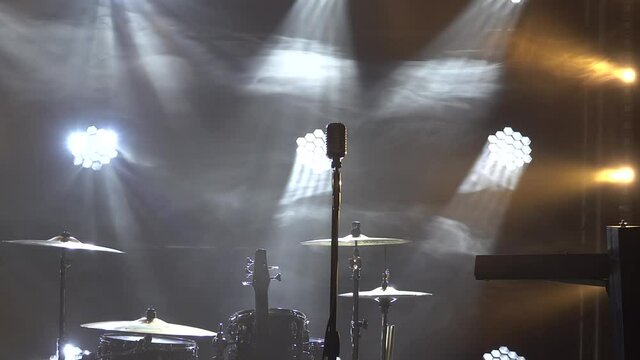 Classic retro chrome microphone and electric guitar together with drums and piano synthesizer keyboard on the stage in dark studio with smoke and neon lighting. Dynamic neon lighting effects. Close up