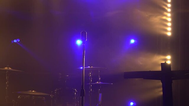 Classic retro chrome microphone and electric guitar together with drums and piano synthesizer keyboard on the stage in dark studio with smoke and neon lighting. Dynamic neon lighting effects. Close up