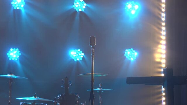 Classic retro chrome microphone and electric guitar together with drums and piano synthesizer keyboard on the stage in dark studio with smoke and neon lighting. Dynamic neon lighting effects. Close up