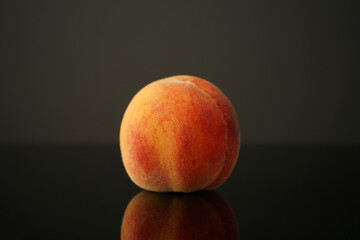 peach lies on the table against a dark background. Beautiful, juicy, ripe and beautiful is reflected in the black glass of the table. Perfect for backgrounds or wallpapers.