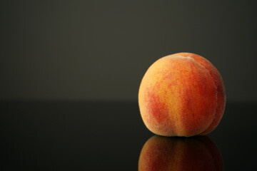 peach lies on the table against a dark background. Beautiful, juicy, ripe and beautiful is reflected in the black glass of the table. Perfect for backgrounds or wallpapers.