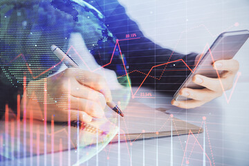 Double exposure of forex graph sketch hologram and woman holding and using a mobile device. Stock market concept.