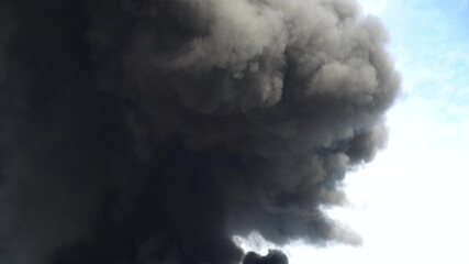 Black smoke rises into the sky. A big chemical fire at a factory building. Thick black smoke covers the sky.