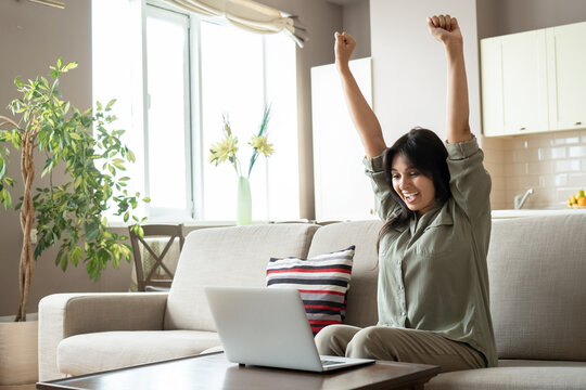 Excited indian woman celebrating online win success looking at laptop at home. Happy euphoric indian lady student, lottery winner raising hands get new job opportunity, watching game on computer.