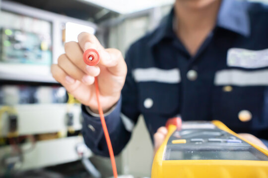The positive end of the multimeter held by an engineer with a blurred background, the concept of using digital tools to check electrical and electronic equipment. Intentional blur image